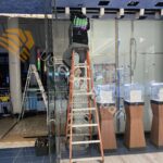A broken storefront glass wall being repaired by a technician using specialized tools and materials in a Virginia retail store.
